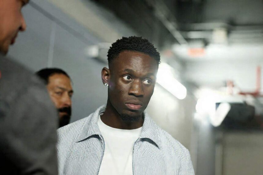 USMNT forward Folarin Balogun of the United States arrives at Fanatics Fest at Javits Center in New York New York on July 17 2026 ahead of a press conference for the FIFA World Cup 2026 Final He wears a light blue striped shirt over a white t shirt and a diamond earring walking through a hallway with other people in the background  trybalnews