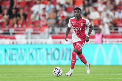 Lamine Camara of AS Monaco wearing a red and white home kit dribbles a football during the Ligue 1 McDonald's match between Monaco and Marseille at Louis II Stadium on August 30, 2026 in Monaco. Fans in red seats are blurred in the background.