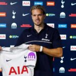 Mykhailo Mudryk unveiled as a new Tottenham Hotspur player after joining on loan from Chelsea The Ukrainian winger smiles while holding up the clubs white home jersey with AIA and Kraken sponsors He wears a navy blue Tottenham polo with Betano on the front and stands in front of a backdrop with Tottenham Nike AIA and other sponsor logos  trybalnews