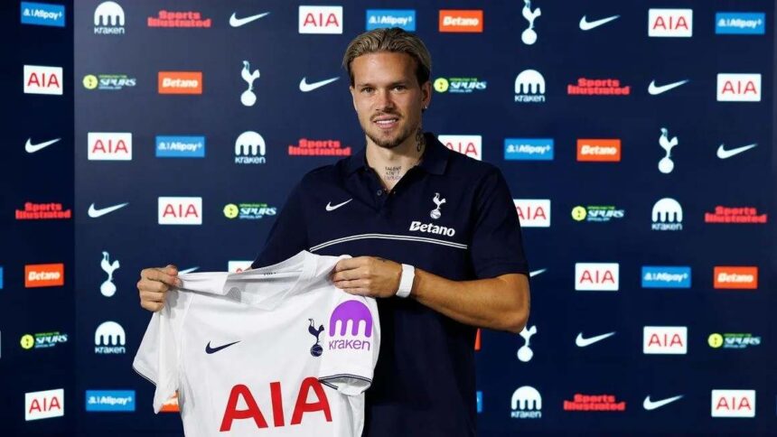 Mykhailo Mudryk unveiled as a new Tottenham Hotspur player after joining on loan from Chelsea The Ukrainian winger smiles while holding up the clubs white home jersey with AIA and Kraken sponsors He wears a navy blue Tottenham polo with Betano on the front and stands in front of a backdrop with Tottenham Nike AIA and other sponsor logos  trybalnews