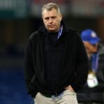 Chairman Todd Boehly of Chelsea FC walks across the pitch with his hands in his pockets after the UEFA Champions League match He is wearing a black zip up jacket over a black shirt light colored pants and a UEFA accreditation lanyard The stadium background is blurred  trybalnews