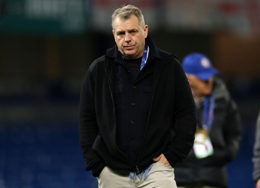 Chairman Todd Boehly of Chelsea FC walks across the pitch with his hands in his pockets after the UEFA Champions League match He is wearing a black zip up jacket over a black shirt light colored pants and a UEFA accreditation lanyard The stadium background is blurred  trybalnews