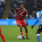 Fulham midfielder Alex Iwobi in red and black checkered away kit controlling ball on pitch during Premier League match against Coventry City wearing black gloves and braided hair  trybalnews