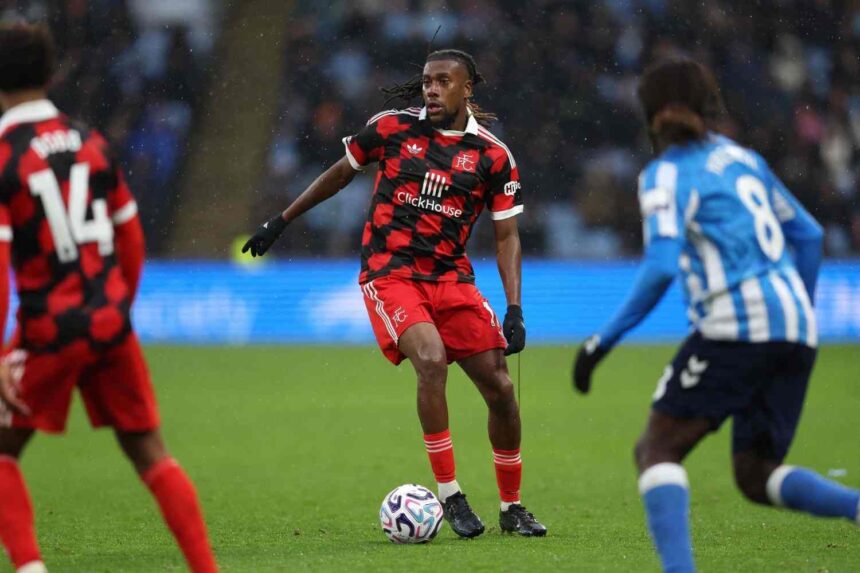 Fulham midfielder Alex Iwobi in red and black checkered away kit controlling ball on pitch during Premier League match against Coventry City wearing black gloves and braided hair  trybalnews