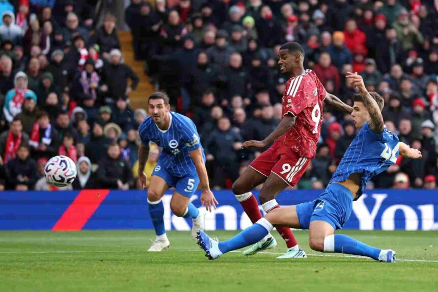 Liverpool striker Alexander Isak in red number 9 kit scores past Brighton defenders in blue kits ball heading towards net during Premier League match at Anfield  trybalnews
