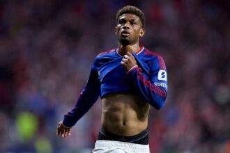 Amad Diallo of Manchester United, wearing the blue long-sleeve away kit with red shoulder stripes, reacts with dejection following his side's defeat, pulling at his shirt while looking up during the UEFA Champions League 2026/27 League Phase MD2 match between Atletico de Madrid and Manchester United at the Riyadh Air Metropolitano on October 13, 2026, in Madrid, Spain.
