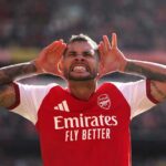 Arsenal midfielder Bruno Guimaraes celebrates with hands cupped around his ears after scoring during a Premier League match at Emirates Stadium He is wearing the red and white Arsenal home kit with visible arm tattoos  trybalnews