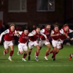 Eight Fleetwood Town players in red and white kits running and shouting in celebration on pitch at night  trybalnews