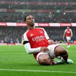 Arsenal defender Gabriel in red Emirates shirt sliding on knees in rain celebrating goal at Emirates Stadium teammates running behind him during Premier League match against Everton  trybalnews