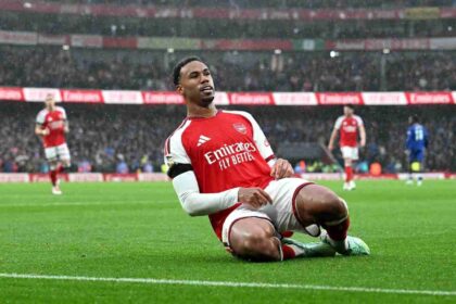 Arsenal defender Gabriel in red Emirates shirt sliding on knees in rain celebrating goal at Emirates Stadium, teammates running behind him during Premier League match against Everton
