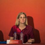 International Olympic Committee President Kirsty Coventry seated at a press conference table during Dakar 2026 wearing a maroon polo shirt with the Olympic rings in front of a red backdrop with sponsor logos  trybalnews