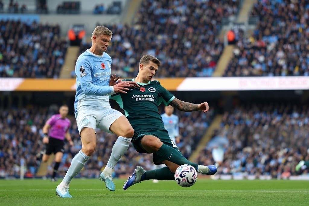 Manchester City vs Brighton Hove Albion Trybal News Manchester City striker Erling Haaland wearing the light blue No 9 kit challenges Brighton defender Luka Vuskovic wearing the dark green No 44 kit for the ball during the Premier League match at the Etihad Stadium with a packed crowd in the background trybalnews