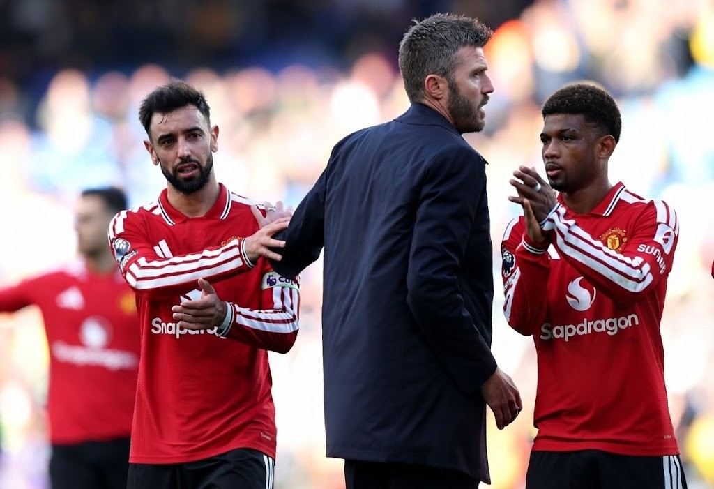 Michael Carrick Trybal News Manchester United captain Bruno Fernandes in red home shirt talking to manager Michael Carrick in dark coat on pitch after Premier League draw against Leeds United at Elland Road with Amad Diallo clapping nearby trybalnews