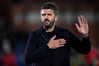 Michael Carrick wearing black jacket with hand on chest and other hand raised apologising to Manchester United supporters after 4-1 Champions League loss to Como 1907 at Giuseppe Sinigaglia Stadium