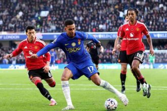 Chelseas Morgan Rogers wearing the blue No 17 kit runs with the ball past Manchester United defenders in red during the Premier League match at Stamford Bridge  trybalnews