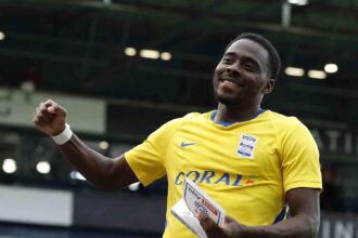 Birmingham City player Bright Osayi-Samuel smiles and raises a fist while holding a Sky Bet Player of the Match trophy. He is wearing Birmingham's yellow away shirt at The Hawthorns stadium.