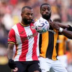Brentford striker Igor Thiago in red and white striped shirt battling with Hull City defender Semi Ajayi in orange and black striped shirt for aerial ball during Premier League match at MKM Stadium  trybalnews