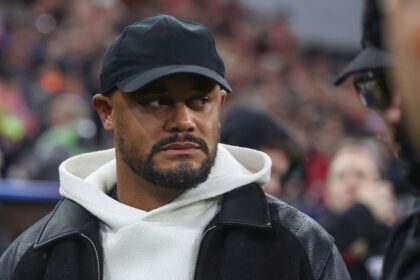 Vincent Kompany wearing black cap, white hoodie and black jacket looking to side before Bayern Munich vs Arsenal Champions League match in Munich.