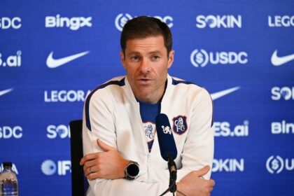 Chelsea manager Xabi Alonso sitting at a table answering questions during a press conference at Chelsea Training Ground in Cobham